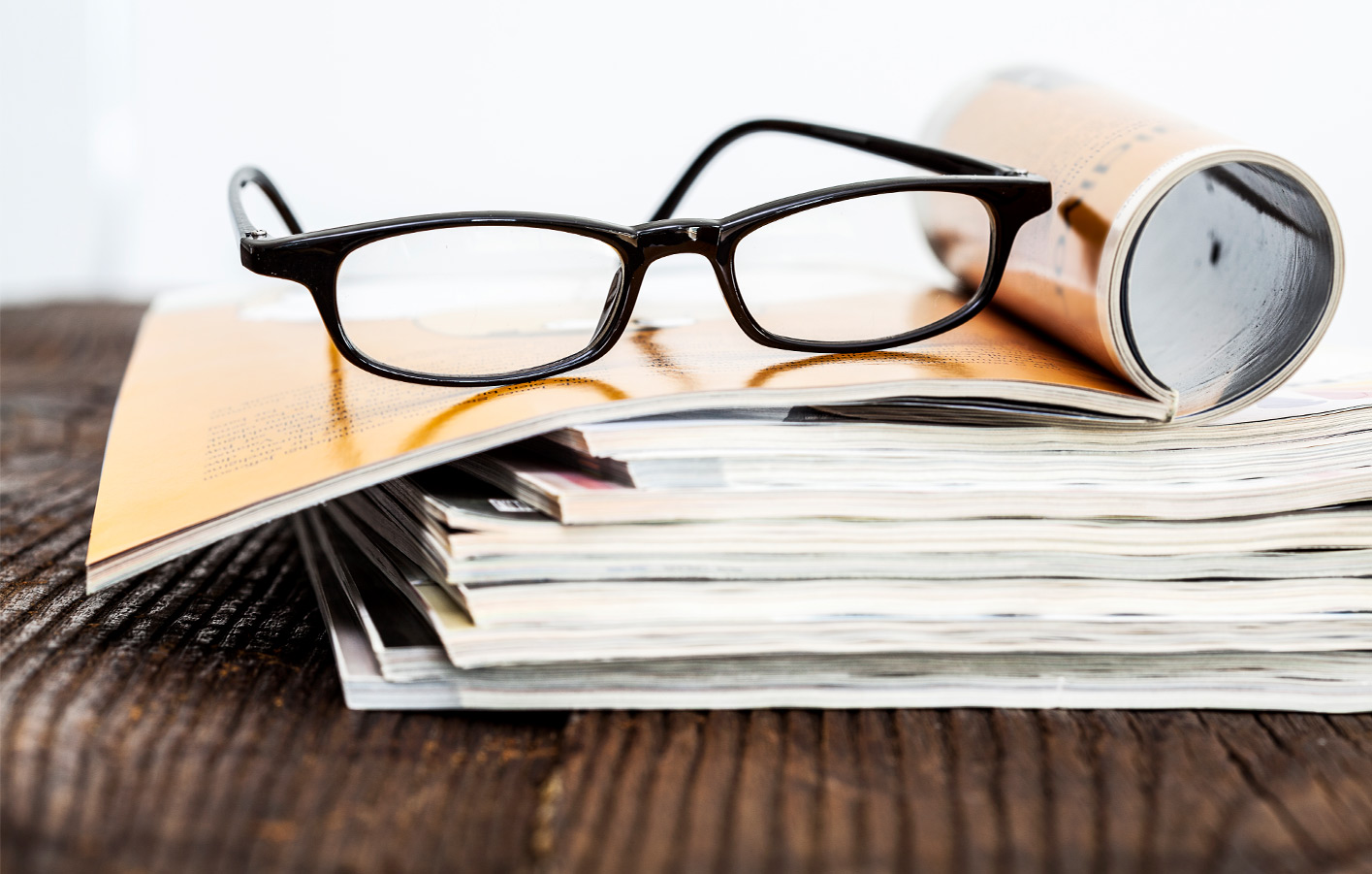 Kataloge auf Holztisch, darauf liegt eine Brille